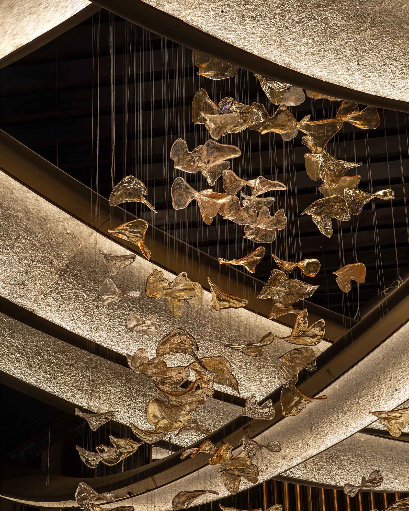 Cascading hand-formed glass lighting installation in a warm architectural interior