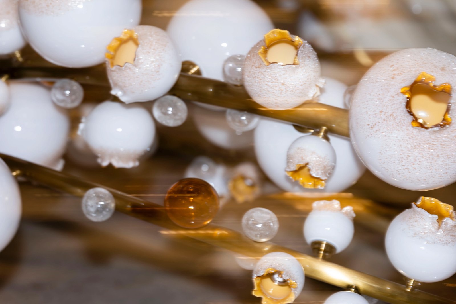 Close-up detail of bespoke white and amber glass lighting on a brass structure